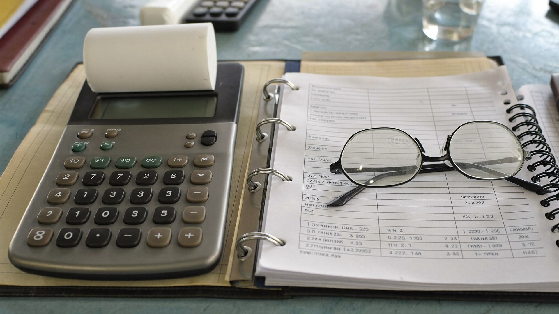 A calculator, a spike file of invoices and a bound ledger on an accounts desk