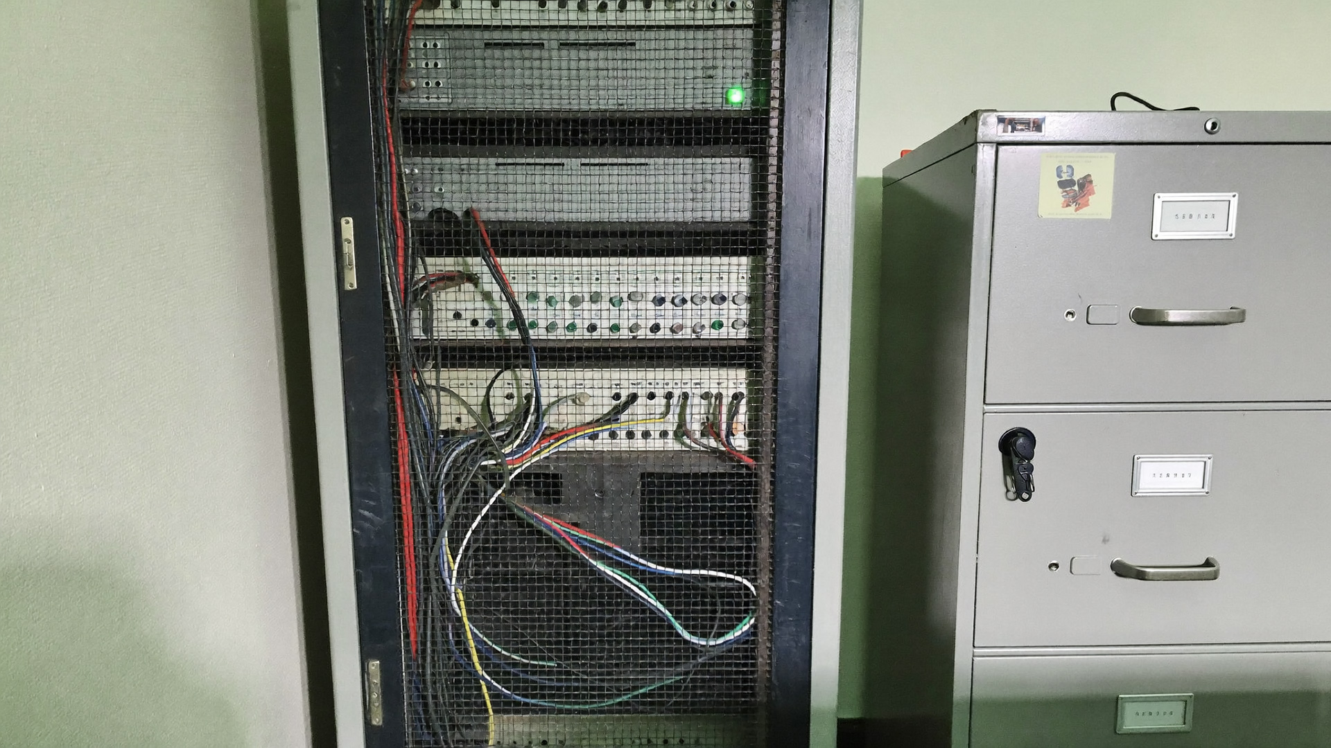 A locked server cabinet beside a steel filing cabinet with the key still in it